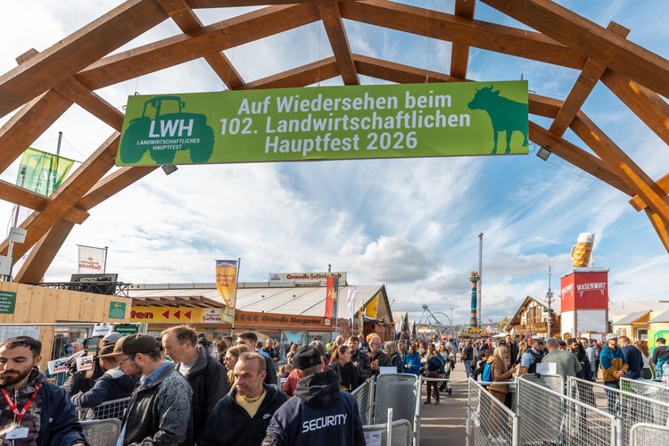 Besucherinnen und Besucher am Einlass des Landwirtschaftlichen Hauptfests 2022 in Stuttgart unter einem Holzbogen mit grünem Banner: „Auf Wiedersehen beim 102. Landwirtschaftlichen Hauptfest 2026“. Im Hintergrund Festzelte und Volksfest-Attraktionen.