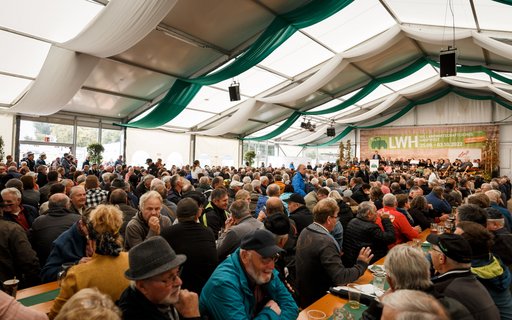 Festzelt mit grün-weißer Decke, viele Menschen schauen auf Bühne mit Banner „LWH Landwirtschaftliches Hauptfest 25.09. – 03.10.2022”. 