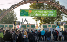 Menschenmenge am Eingang des 100. Landwirtschaftlichen Hauptfests unter einem großen grünen Banner mit der Aufschrift ‚Herzlich Willkommen auf dem 100. LWH!‘. Im Hintergrund befinden sich Infostände und Bäume.