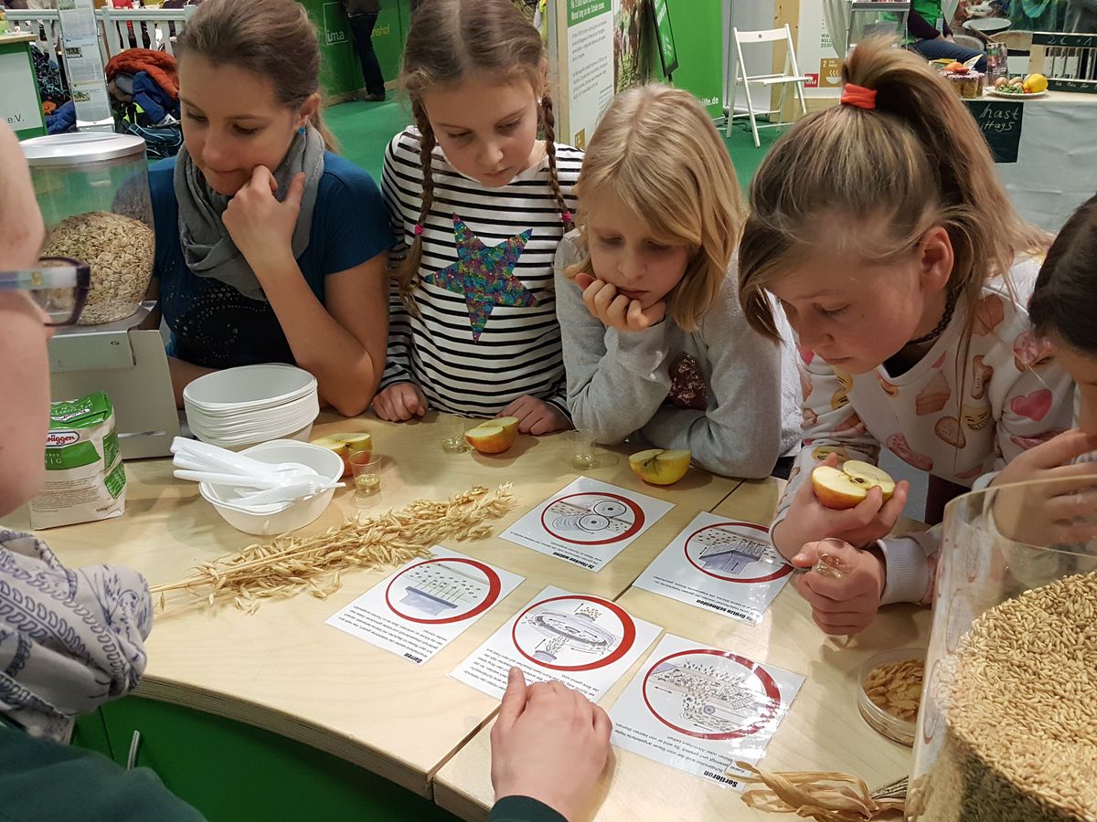 Kinder sitzen an einem Tisch und basteln bei einer Mitmachaktion auf einer Messe oder Ausstellung.